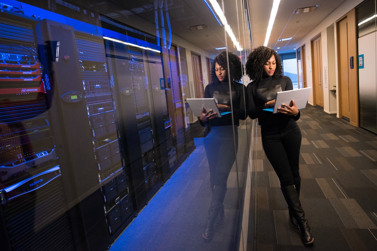 A person standing in a darkened room facing a wall of large screens filled with charts and data.