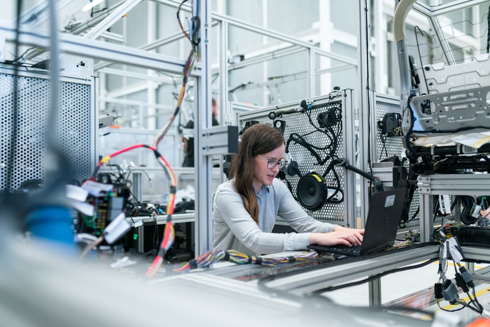 An engineer working at a bench in a bright industrial laboratory beside machinery.