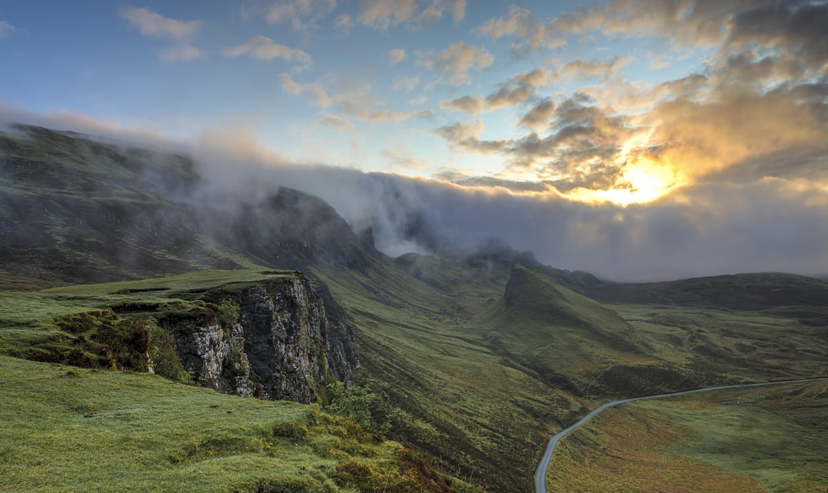 Mist lying in a green valley between low hills at sunrise.