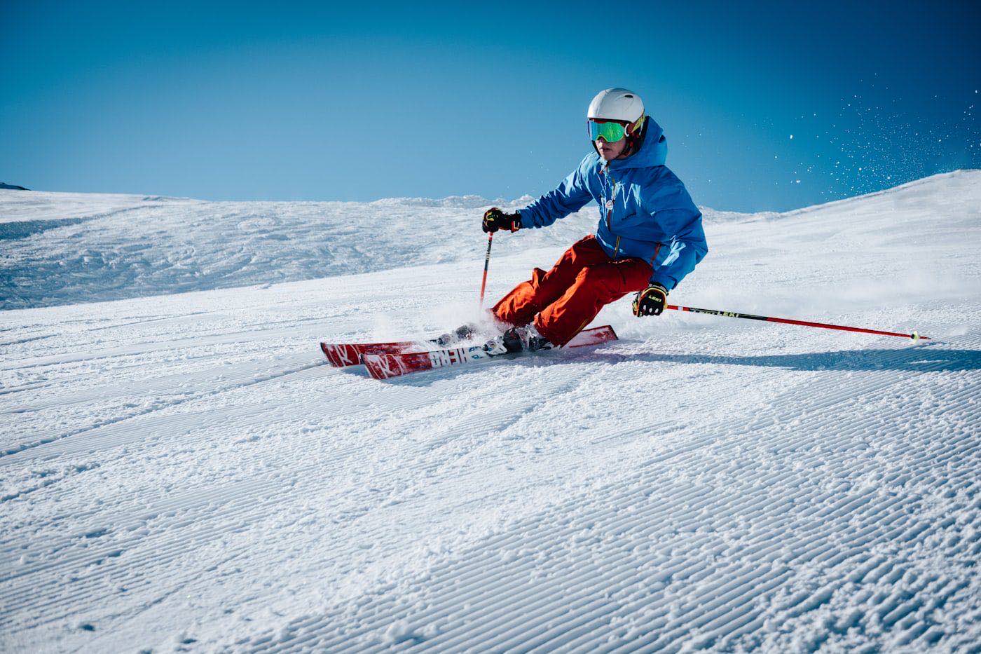 A skier in a red jacket carving a turn on a groomed slope, spraying snow.
