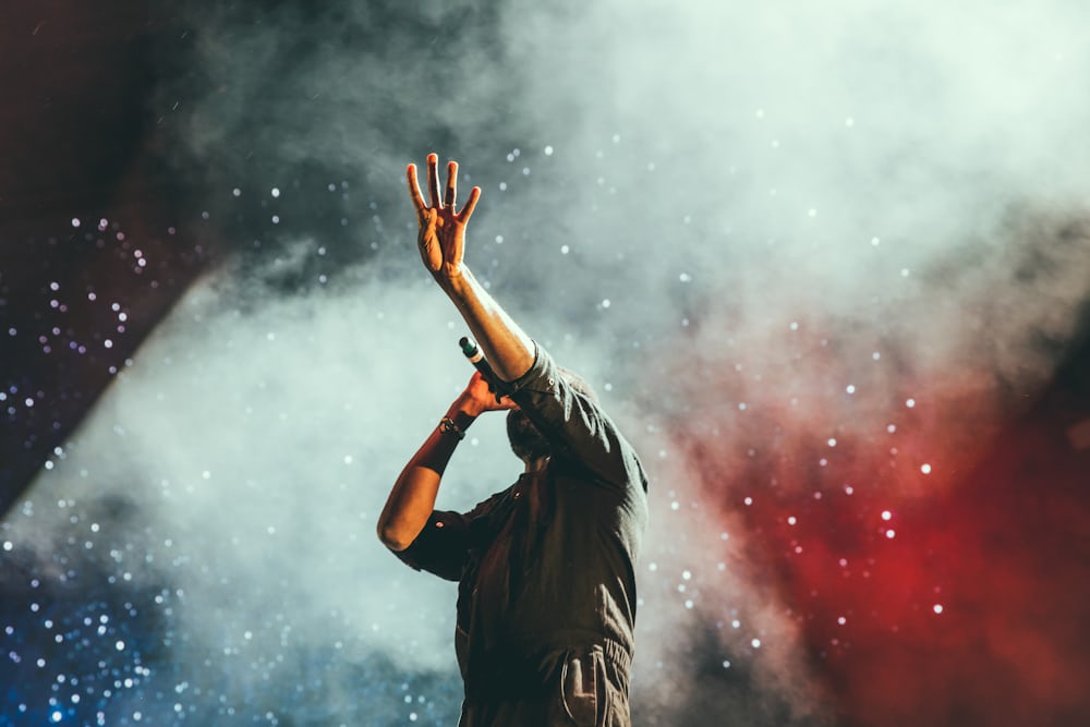 A figure with raised arms silhouetted in bright stage light and haze.