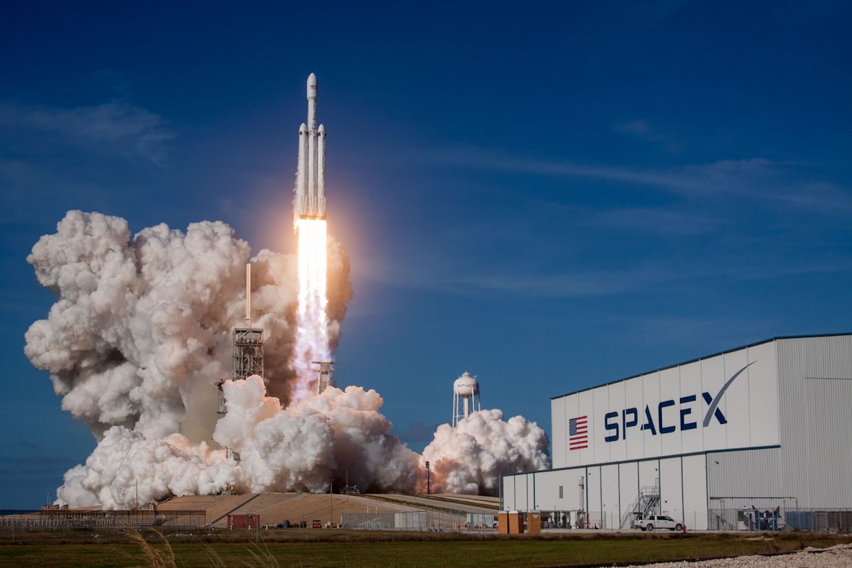 A rocket lifting off from a launch pad on a bright column of exhaust against a blue sky.