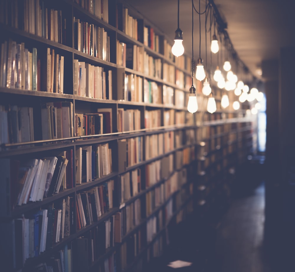 Rows of library shelves packed with books, lit by warm hanging lamps.