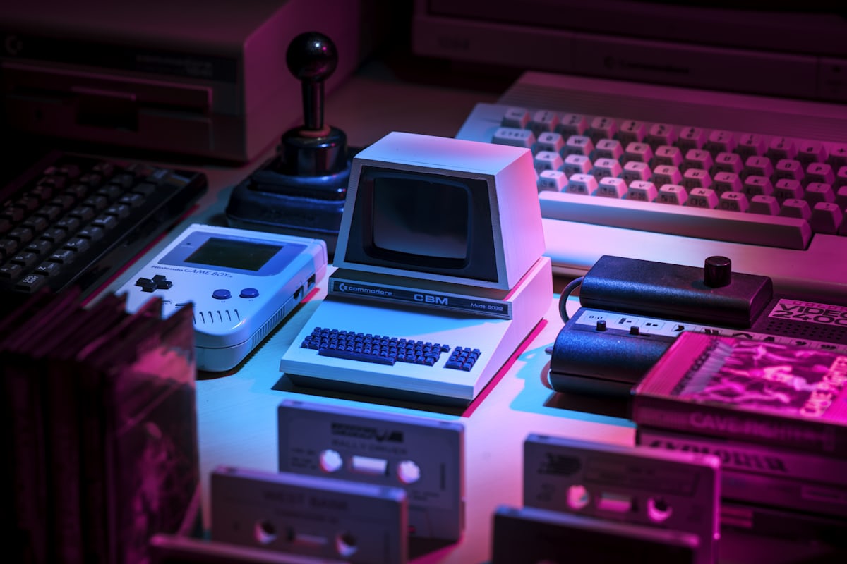 Vintage desktop computers arranged in a row and lit with pink and blue neon light.