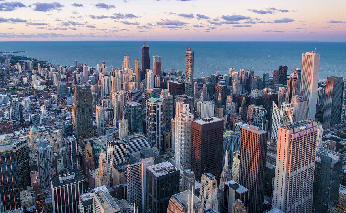 An aerial view of a dense city skyline of tall towers seen from above at dusk.